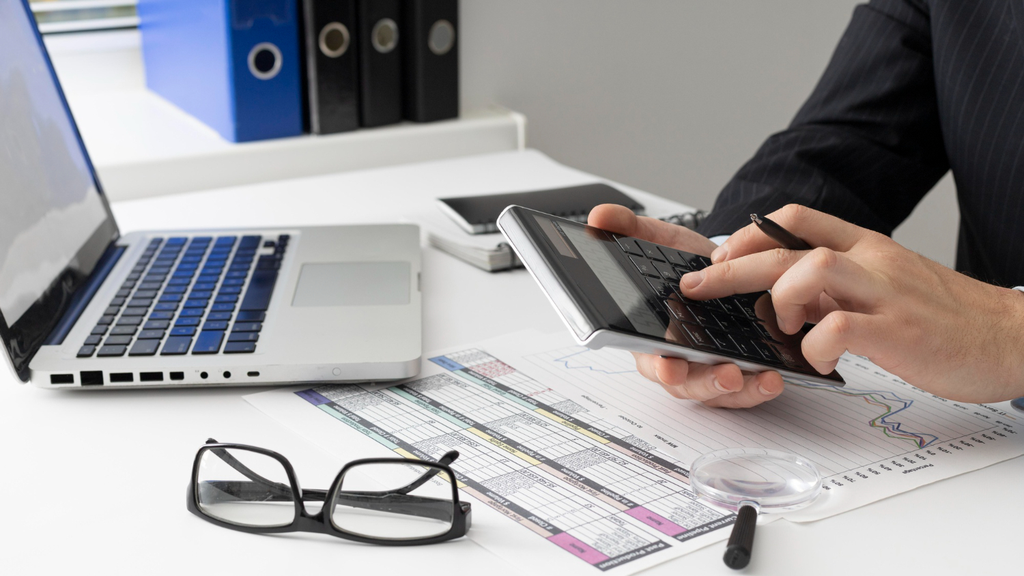 An image of an accountant holding a calculator while facing his laptop
